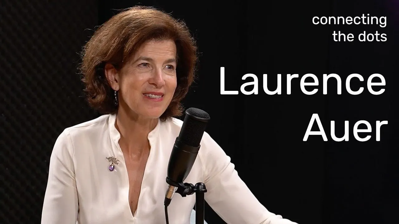 Ambassador Laurence Auer speaks into a microphone against a black backdrop displaying her name.