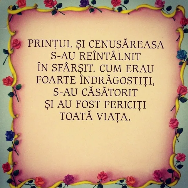 A pink cake with a yellow ribbon border and small roses, topped with Romanian text about the prince and Cinderella marrying.
